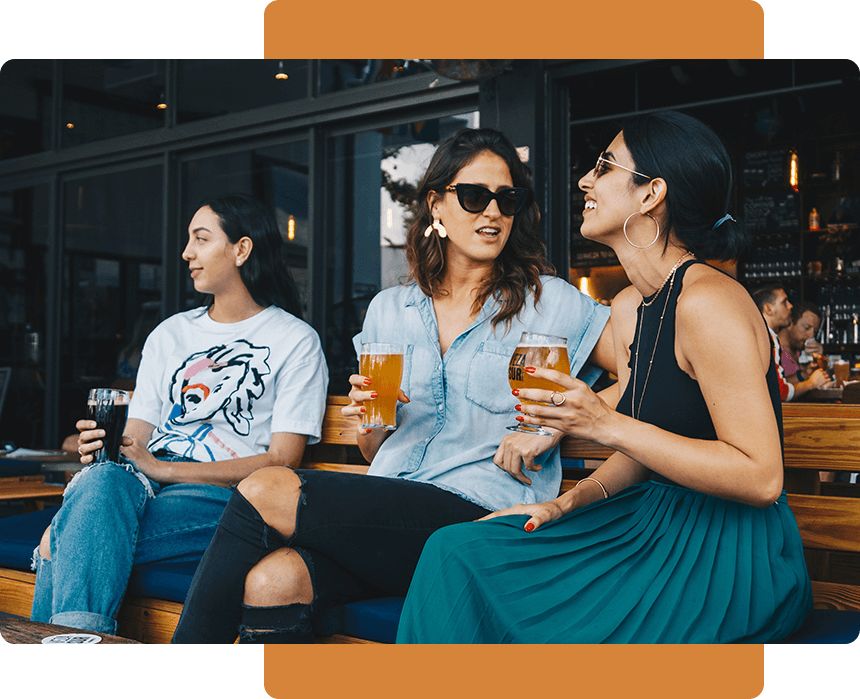 Three people sitting on a bench with drinks.